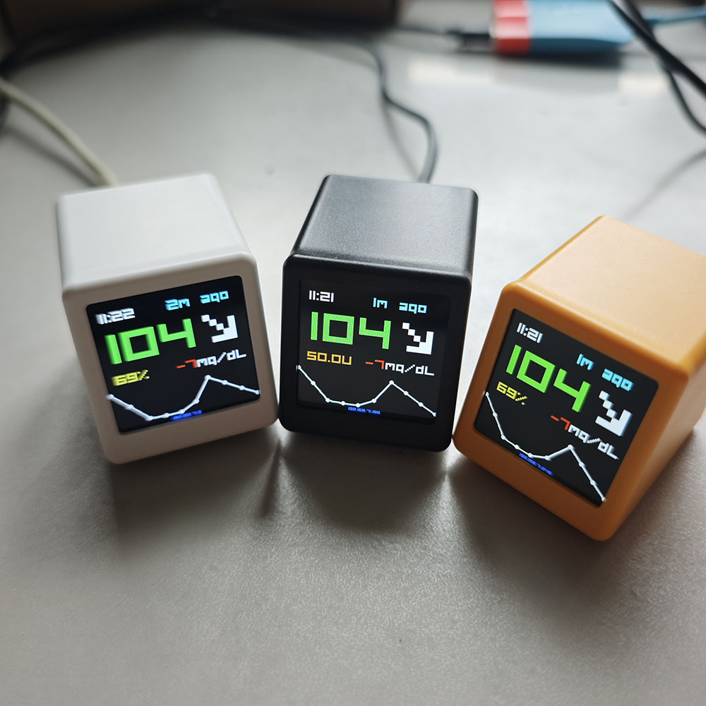BGMate mini in amber on a desk, showing 104 mg/dL with a falling trend arrow